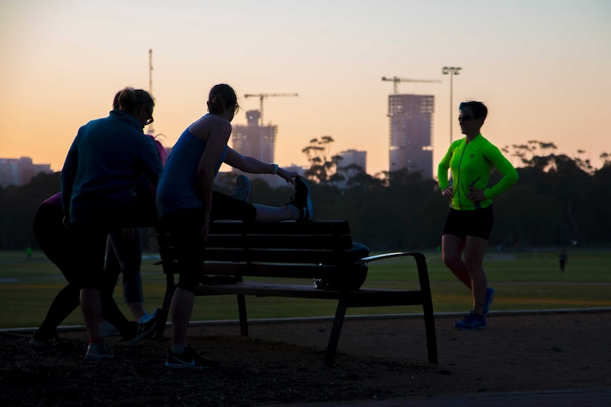 A group of women stretch their legs next to a park bench