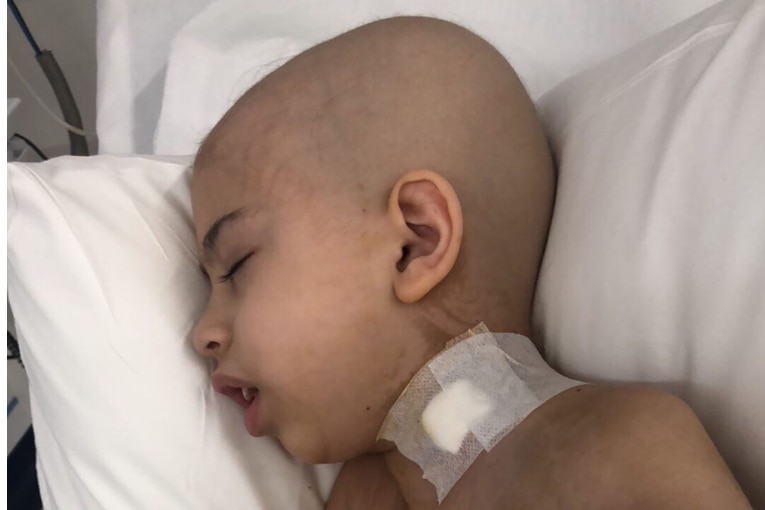 A boy with a shaved head asleep in a hospital bed.