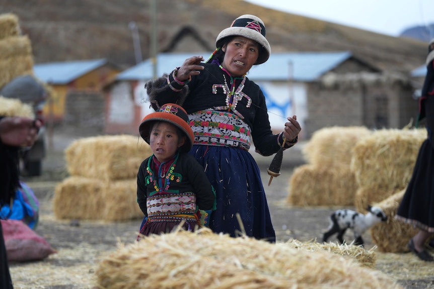 A mother and daughter stand behind bales of hay. 