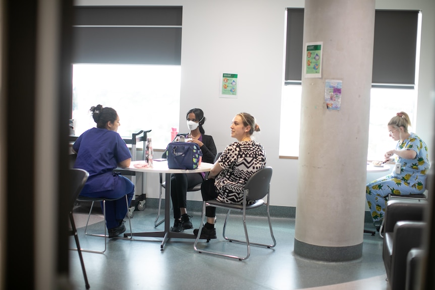 Three midwives in scrubs sit around a table in the break room.