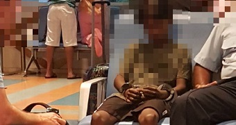 A young boy sitting in an airport lounge, handcuffed.