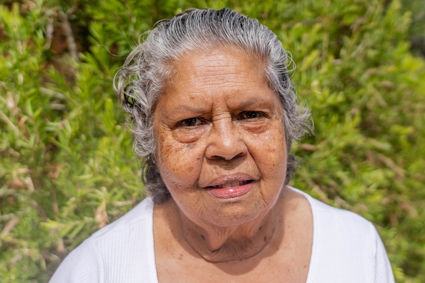 A close up of a woman's face with a bush behind her.