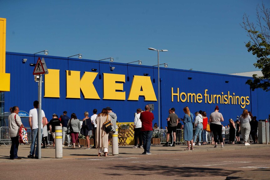 A large group of people standing at a distance from each other on a bright, sunny morning in front of Ikea store.