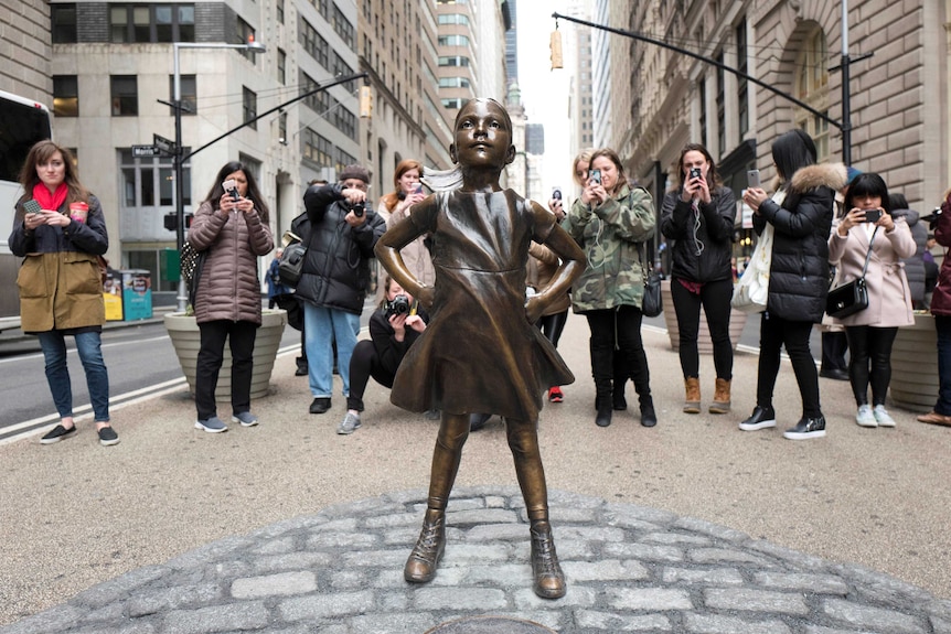 A crowd gathers behind a statue titled Fearless Girl at Wall Street.