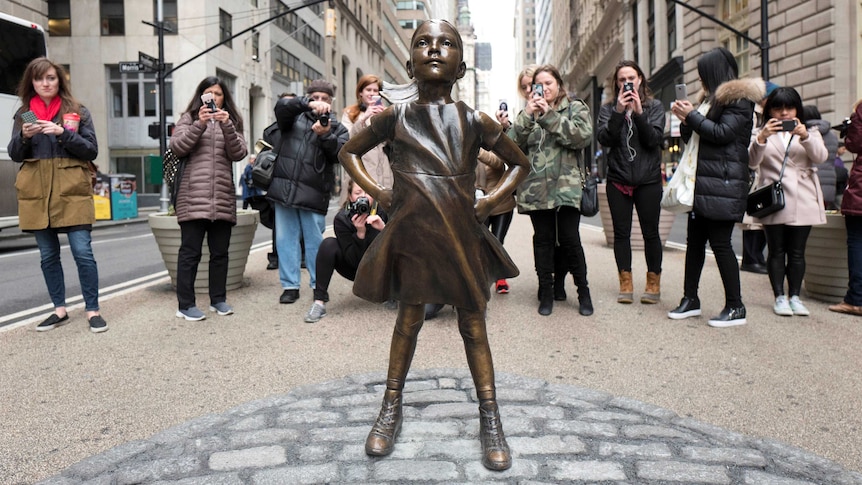 A crowd gathers behind a statue titled Fearless Girl at Wall Street.