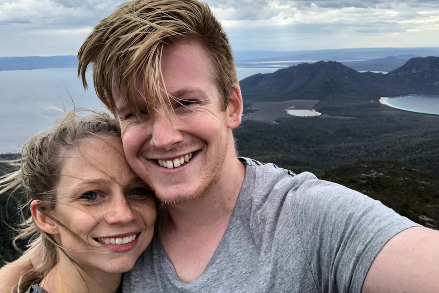 Sarah Robson and Sam Martin posing for a selfie on a hilltop overlooking the ocean.