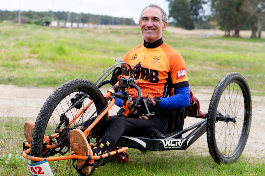 A man sitting in a three-wheel adaptive bike looking at the camera and smiling 