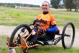 A man sitting in a three-wheel adaptive bike looking at the camera and smiling 