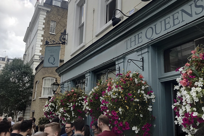 The front of an English Pub covered with hanging flower baskets and crowds in the foreground.