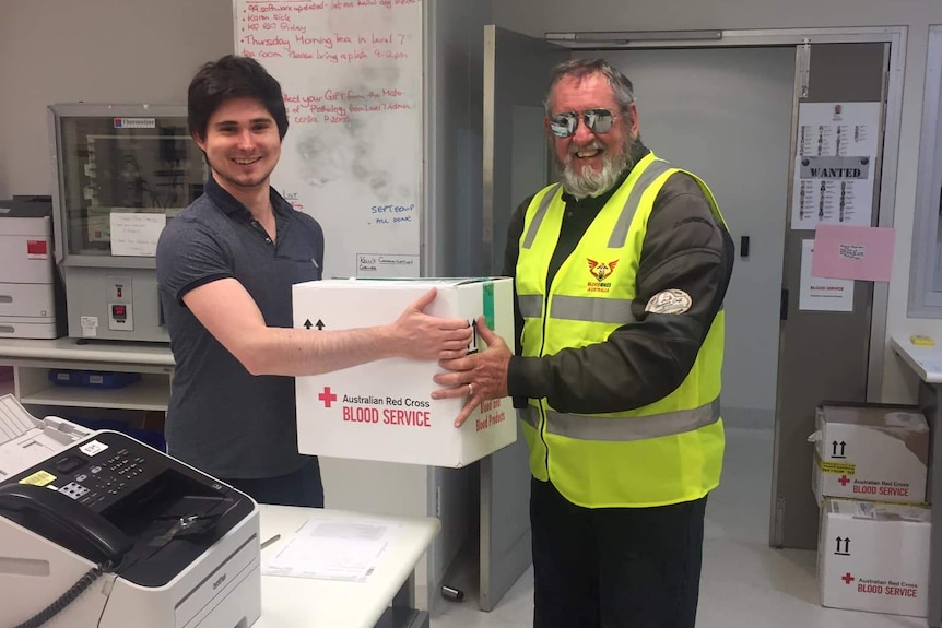 A man in a yellow vest is passed a parcel by a healthcare worker.