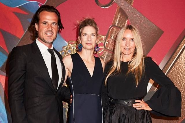 Three people stand on the red carpet.