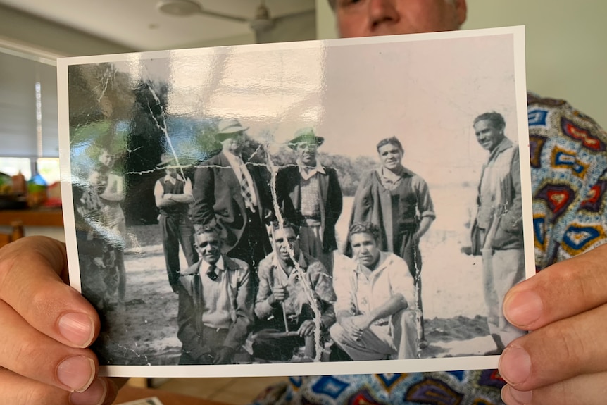 John Patten holds up a creased black and white photo showing a group of Aboriginal men in 1938.