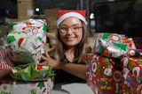 Kaitechia Griffey smiles at the camera wearing a Santa hat. Around her is wrapped gifts, ready for Christmas.
