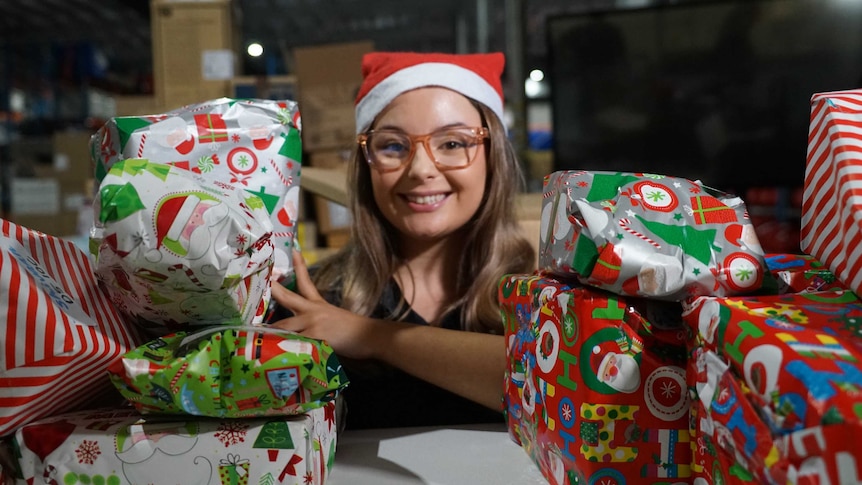 Kaitechia Griffey smiles at the camera wearing a Santa hat. Around her is wrapped gifts, ready for Christmas.