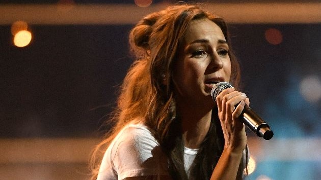 Amy Shark sings into a microphone while performing on stage.