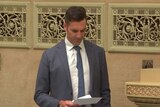 MP Fraser Ellis standing as he reads from a sheet of paper in parliament