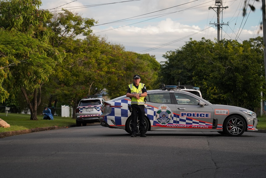 A police officer standing on a road wearing a yellow high viz vest in front of a police car.