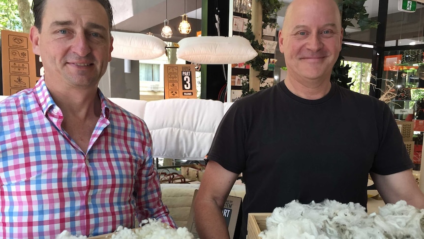 two men hold wooden boxes of wool in front of some floating doonas and pillows in a Sydney shop