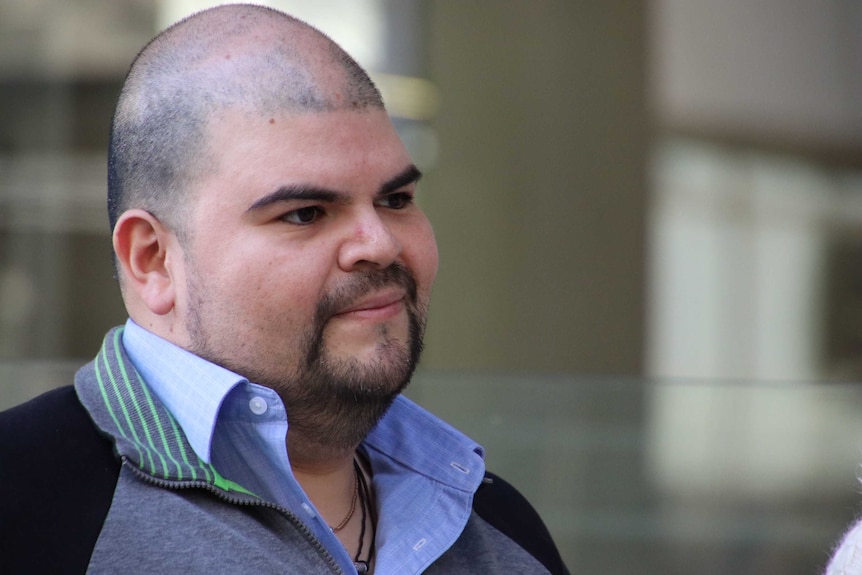 A close up photo of Mauricio outside the court. He has short stubble and a shaved head, and is balding on top.