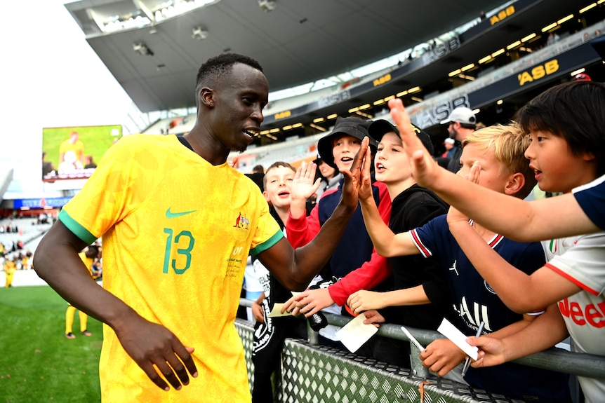 A male soccer player wearing yellow and green high-fives some kids after a game