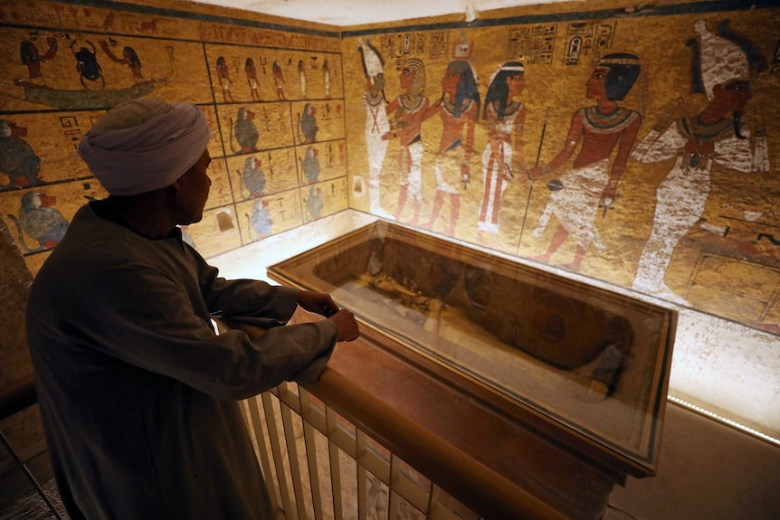 A guard looks at ancient Egyptian drawings and the sarcophagus in Tutankhamun's tomb.
