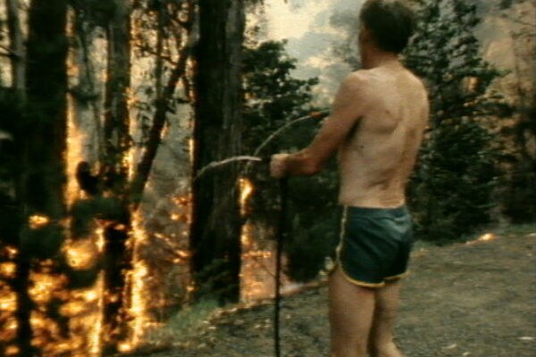 A man in shorts and no shirts hosing a bushfire in a vintage shot from 1983