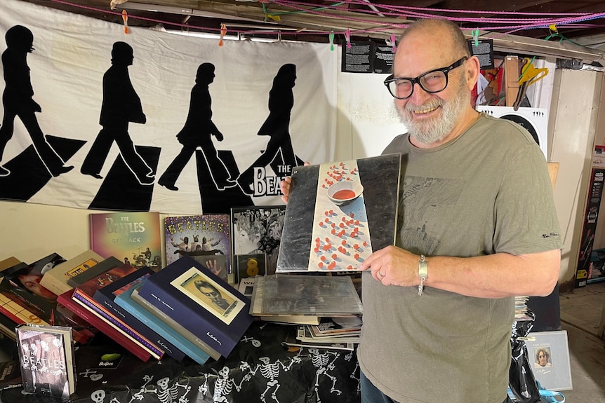 A man holding a Beatles record in front of a table full of Beatles memorabilia