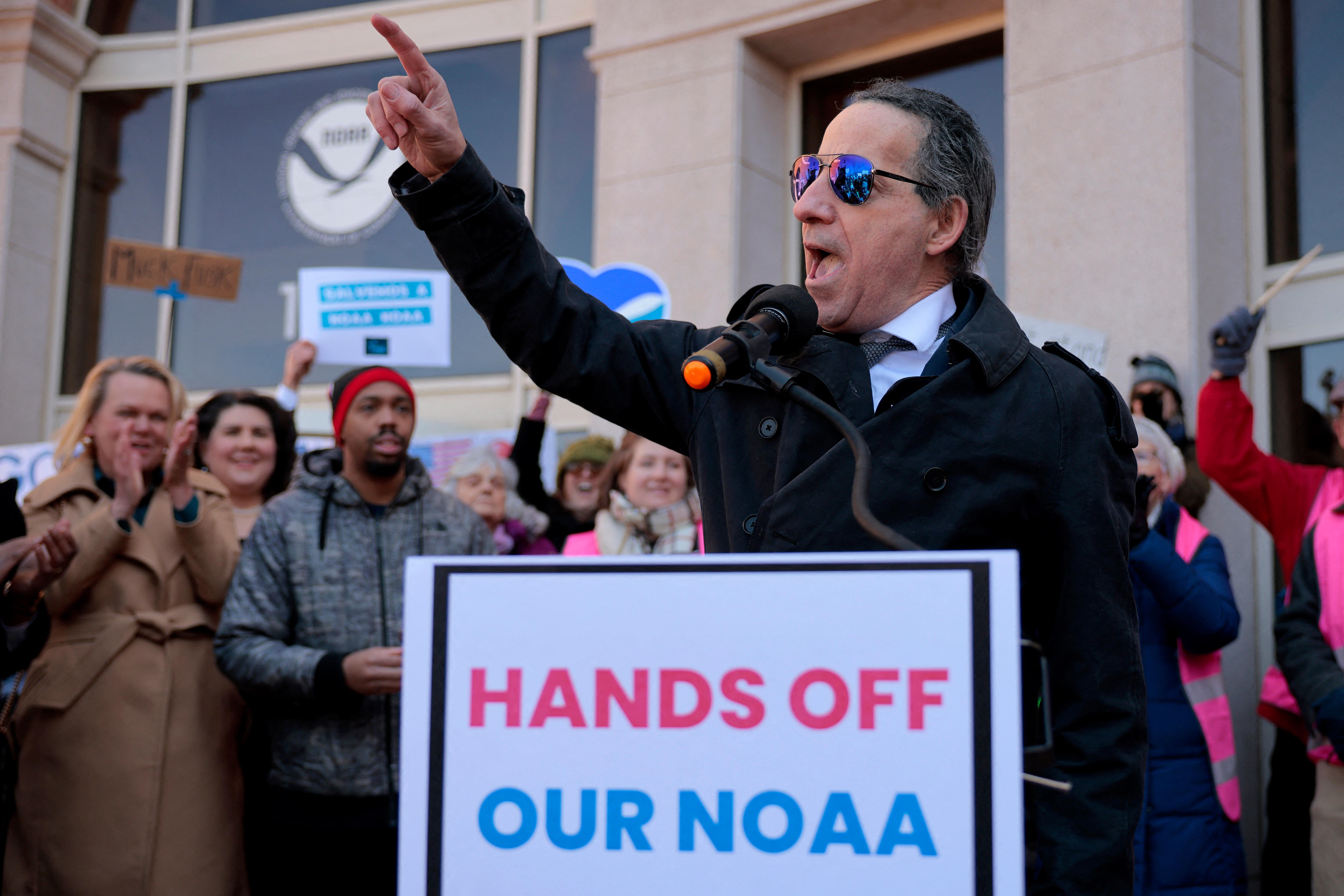 A man on a podium with a sign saying Hands off our NOAA with his arm stretched out 