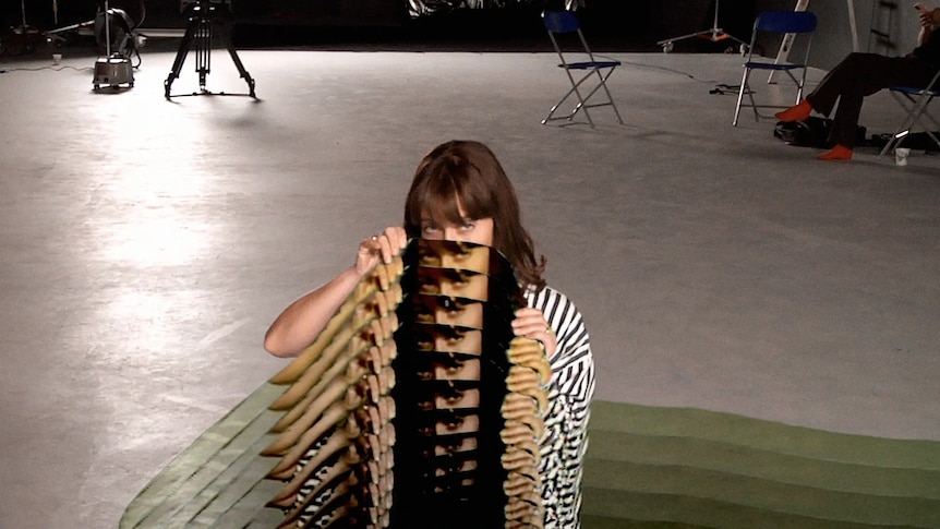Feist sits on a soundstage holding a cut-out that multiplies her outline over and over again