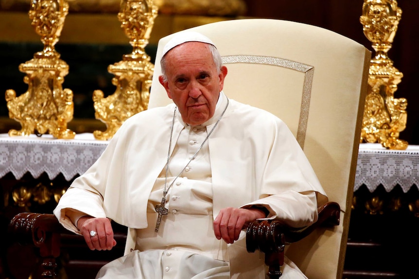 The Pope sits in a wooden chair.