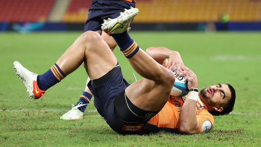 Tom Wright holds onto a rugby ball while lying on his back with his eyes closed and legs in the air