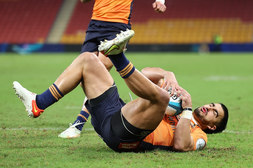 Tom Wright holds onto a rugby ball while lying on his back with his eyes closed and legs in the air