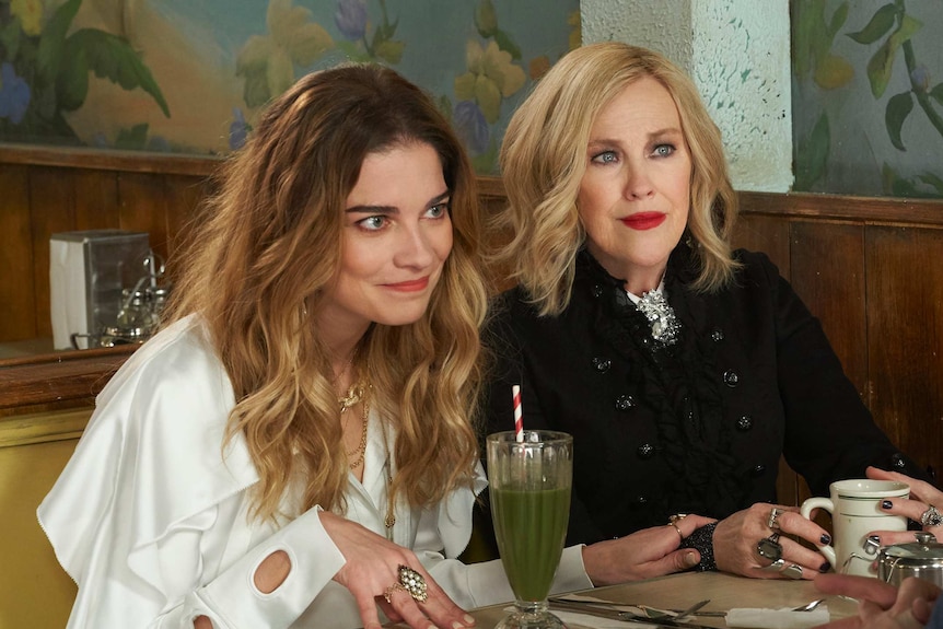 Alexis and Moira sitting at a table in the cafe in the TV show Schitt's Creek