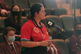 An image of Year 12 student Nickeisha at a microphone in auditorium