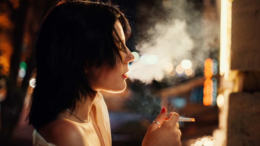 Young woman smoking a cigarette in the street at night
