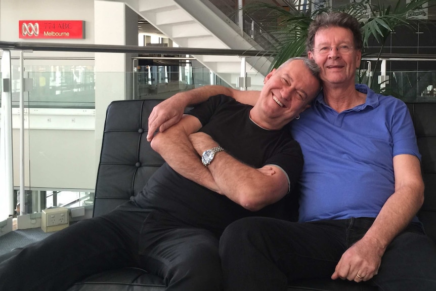 Jimmy Barnes and Red Symons sit together on a couch, smiling and embracing.