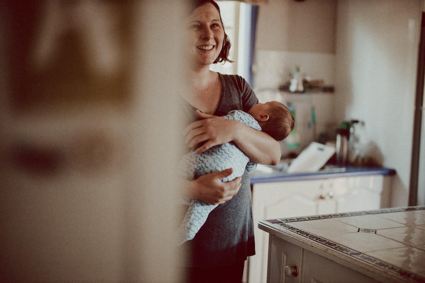 A mother holding her baby in the kitchen.