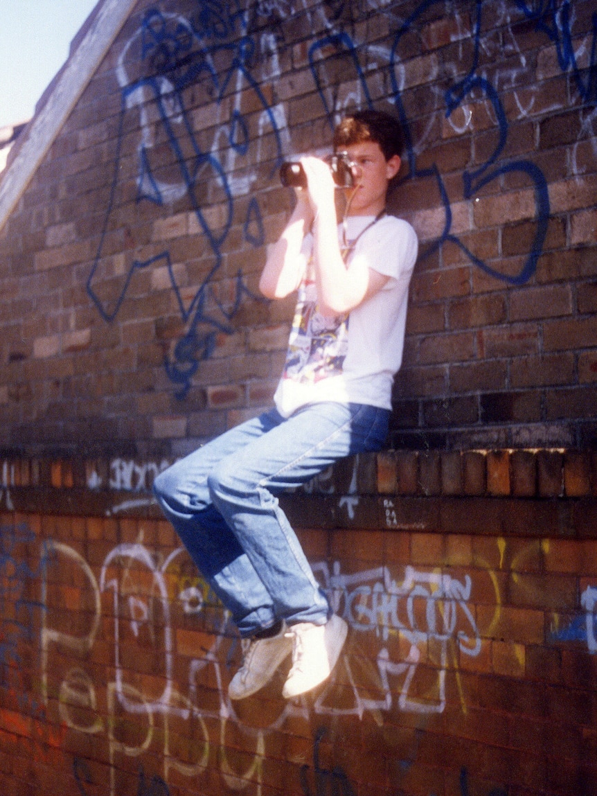 A teenage boy sits on a brick ledge taking a photograph