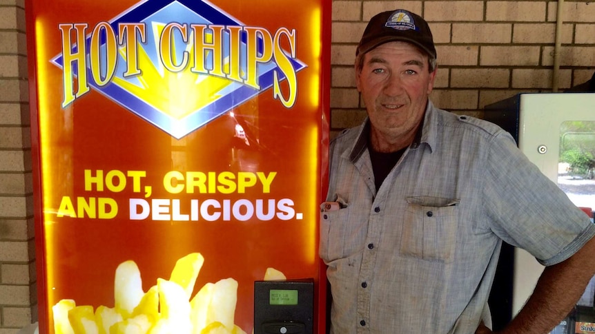 A man stands next to a hot chip vending machine.