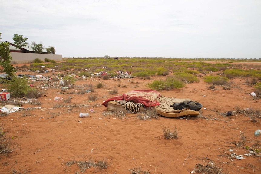 A dirty mattress, sheets and rubbish sit on a patch of scrub and desert on the edge of South Hedland