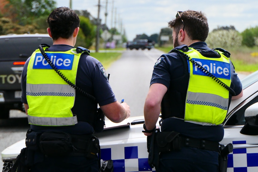 Police officers stand near a car blocking a rural road.