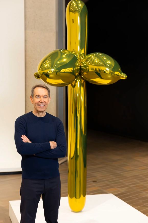 An artist in front of a gold balloon sculpture.
