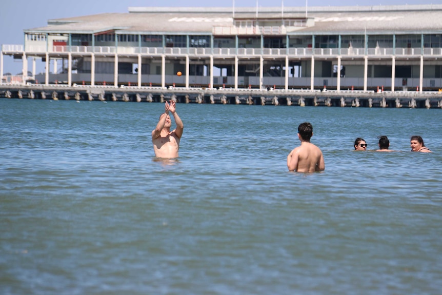 People throw a ball around in the water at Port Melbourne beach.