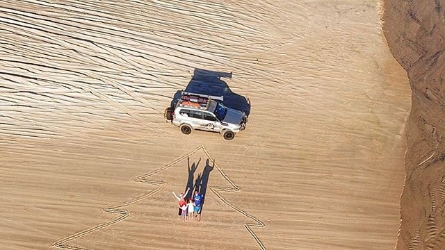 A drone photo a Christmas tree drawn in the sand at a beach.