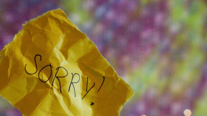 Scrunched up yellow paper with the word "Sorry" written on it with blurred purple and green background