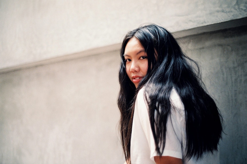 Colour photo of writer Jamie Marina Lau standing in front of concrete wall in the day.