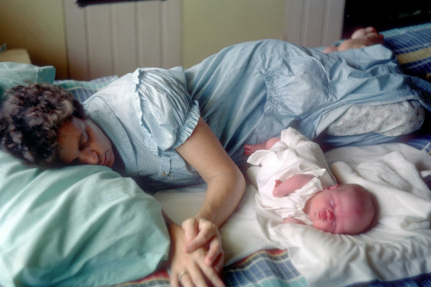 Lisa McManus, as a baby, sleeps on a bed next to her mother.