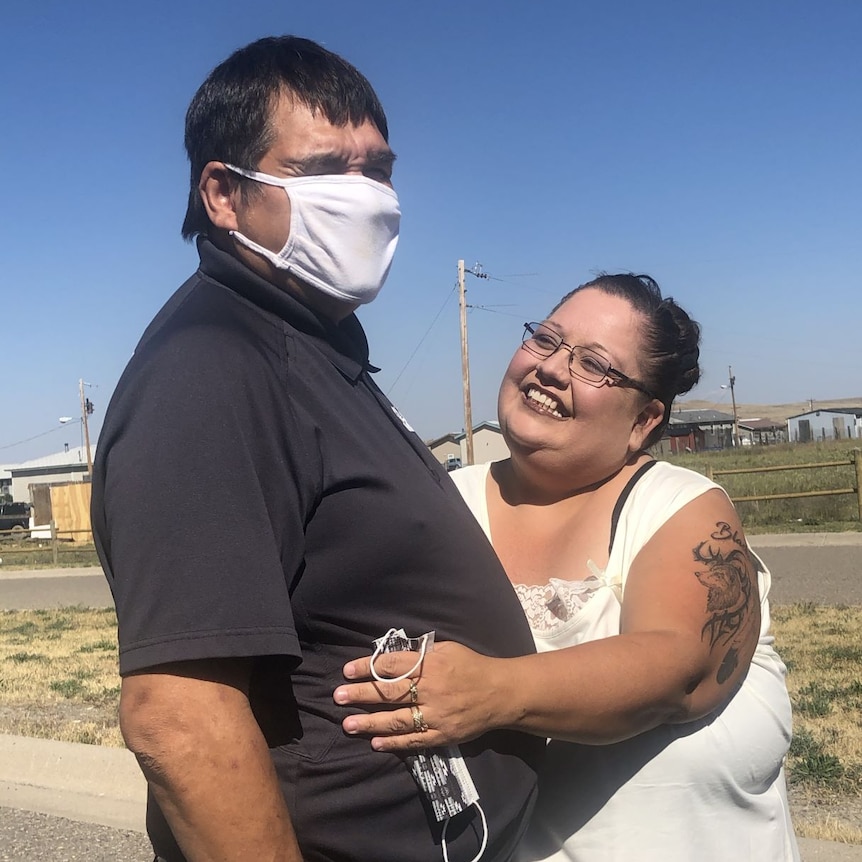 Man wearing a face mask and black shirt standing with a woman who is smiling.