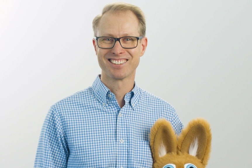 A blond man with glasses holding a kangaroo puppet