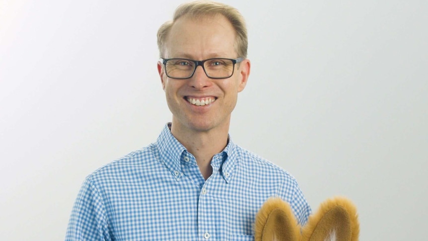 A blond man with glasses holding a kangaroo puppet